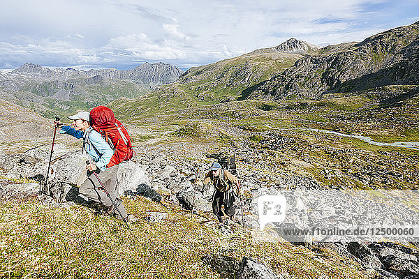 Man And Woman Hiking Up A Steep Hill In Talkeetna Range In Alaska  Usa