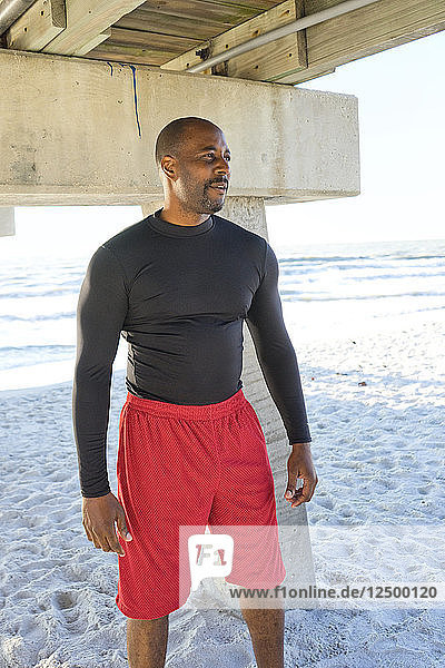 Man in fitness clothes standing under a pier on the beach