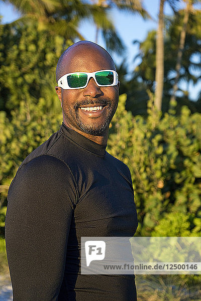 Sportlicher Mann mit Sonnenbrille in einer tropischen Umgebung  der in die Kamera lächelt