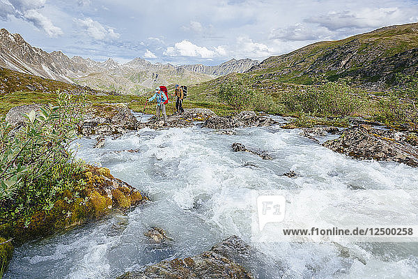 Ein Mann und eine Frau überqueren einen Fluss in Talkeetna Range in Alaska  USA