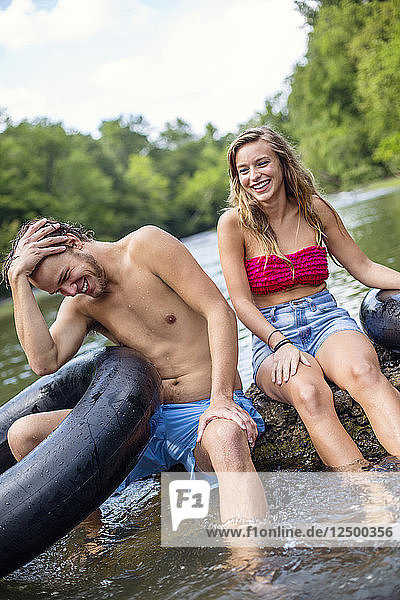 Ein junger Mann und eine Frau lachen  während sie sich auf einem Wasserfall ausruhen  nachdem sie einen Fluss hinuntergerutscht sind.