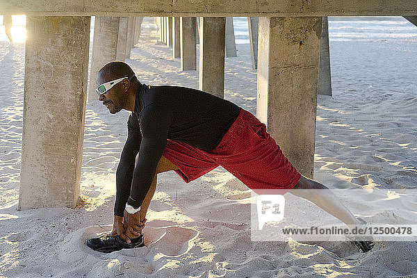 A man stretching in the sand under a beach pier