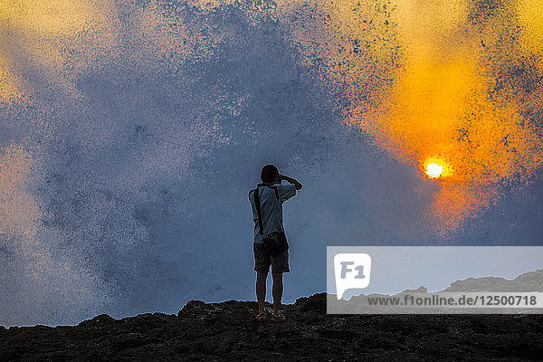 Silhouette eines jungen Fotografen an der Meeresküste bei Sonnenuntergang.
