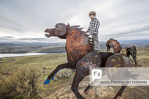Ein Junge  der auf einer Pferdeskulptur in der Stadt Vantage im östlichen Washington steht