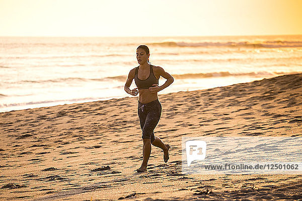 Frau läuft am Strand bei Sonnenuntergang