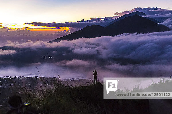Mann fotografiert mit Smartphone in den Bergen bei Sonnenaufgang