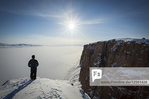 Person Standing On Snowy Cliff In Arctic Bay