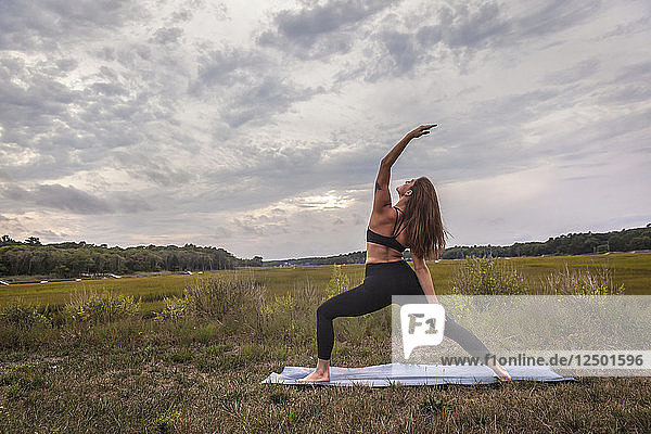 Schöne junge Frau in Reverse Warrior Yoga Pose bei Sonnenuntergang