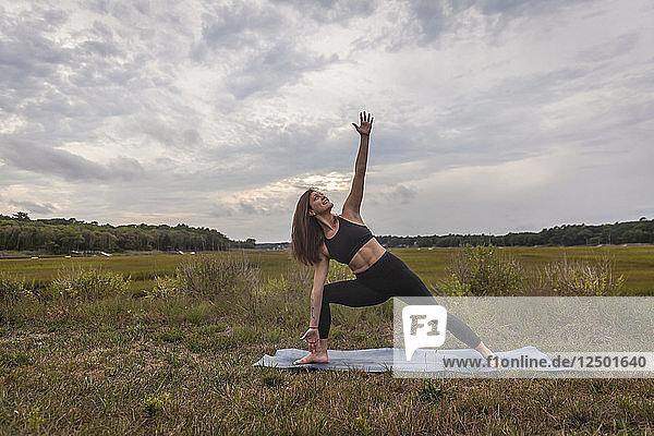Schöne junge Frau streckt sich zum Himmel und macht Yoga bei Sonnenuntergang