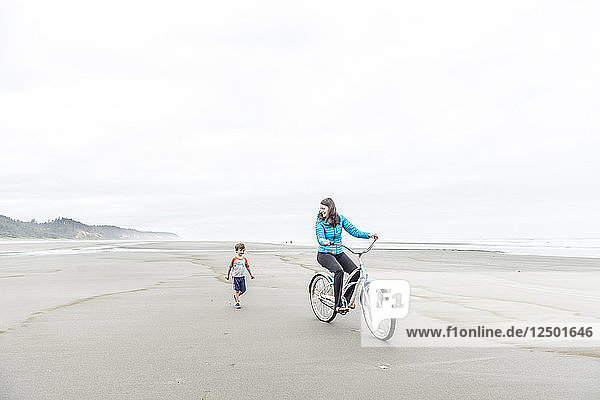 Eine Frau fährt mit dem Fahrrad neben ihrem Sohn an einem Strand im Bundesstaat Washington.