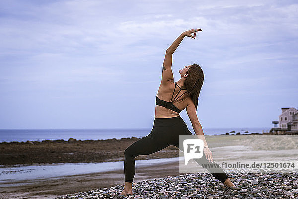 Schöne junge Frau in Reverse Warrior Pose Doing Yoga bei Sonnenuntergang