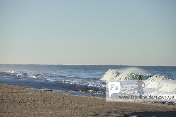 Eine erwachsene Frau läuft spielerisch entlang der brechenden Wellen in Todos Santos  Mexiko