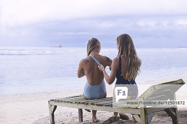 Eine Frau  die den Riemen des Badeanzugs ihrer Freundin am Strand anpasst