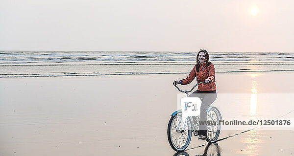 A woman rides a bike on a Pacific Northwest beach at sunset.