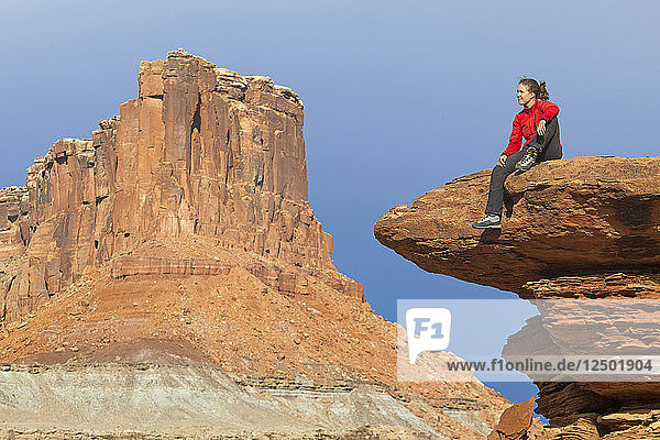 Eine Frau sitzt auf einer Felsenterrasse am Saddle Horse Bottom unterhalb hoher Canyonwände im Canyonlands National Park  Utah.