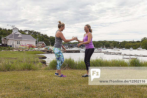 zwei Frauen lachen und machen draußen ein Partner-Workout