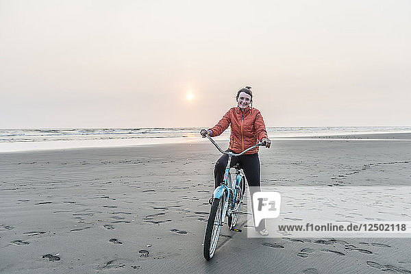 A woman rides a bike on a Pacific Northwest beach at sunset.