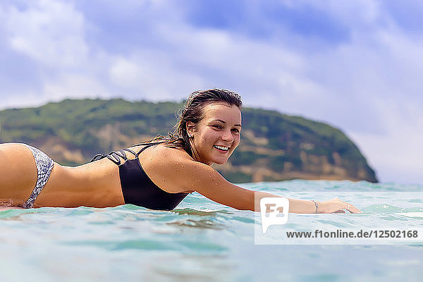 Portrait of young woman lying on surfboard in water
