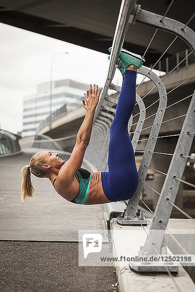 Fit Blonde Frau Doing A Hanging Sit-up auf einer Brücke