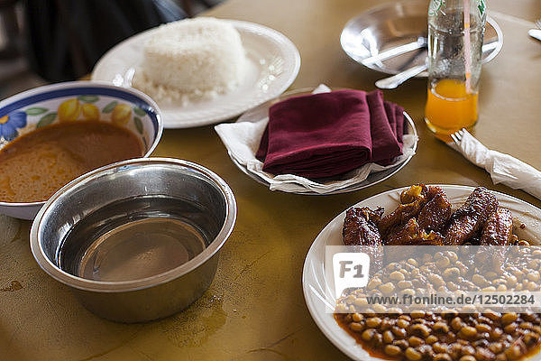Typisches Mittagessen in Accra  Ghana  bestehend aus Reis  Bohnen  rot-rot  Huhn und einer Wasserschüssel zum Händewaschen.