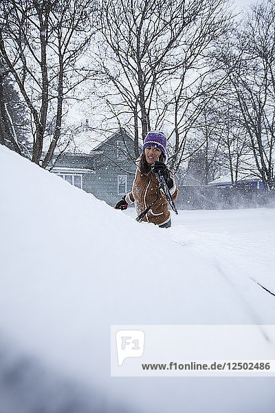 Eine erwachsene Frau  die Spaß daran hat  ihr Fahrzeug nach einer frischen Schneedecke abzuräumen