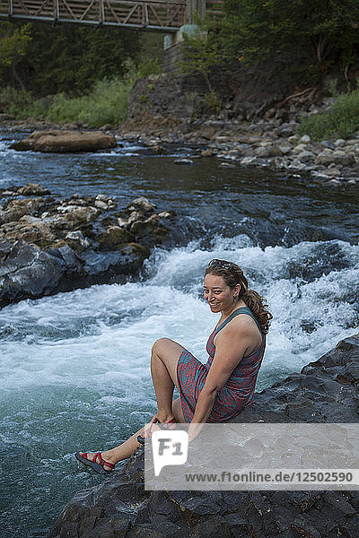 A woman sits on the basalt bank of the Spokane River in Riverside State Park  Washington.