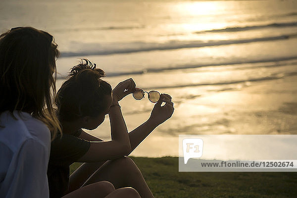 Zwei Frauen sitzen bei Sonnenuntergang am Strand