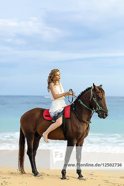 Junge Frau reitet auf einem Pferd am Strand