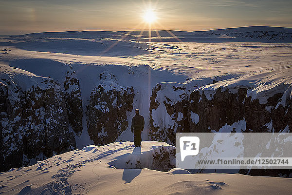 Person Standing On Snowy Cliff In Arctic Bay