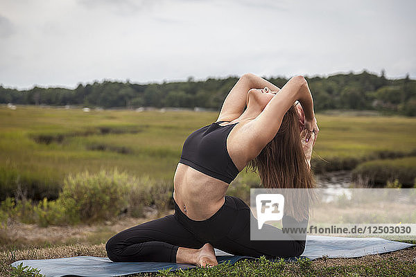 Schöne junge Frau in King Pigeon Yoga Pose auf einer Yoga-Matte bei Sonnenuntergang