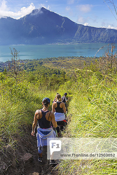 Rear View Of Hikers Hiking In Grass Field Of Bali Island