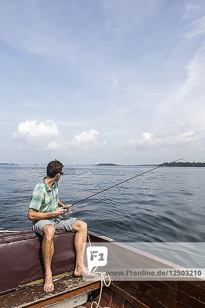 Man Fly Fishing Sitting On The Edge Of Wooden Boat In The Saint Lawrence River