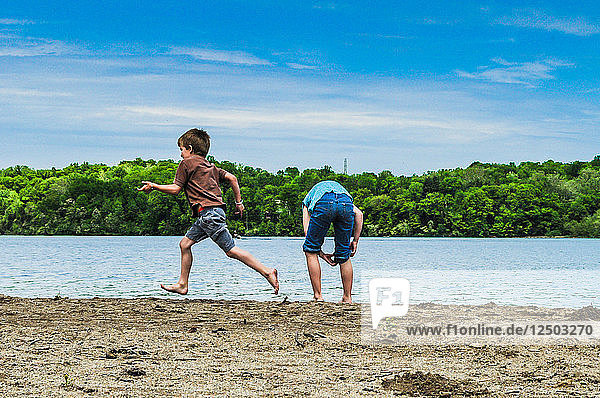A boy runs by a girl at the water's edge at Hueston Woods State Park OH.