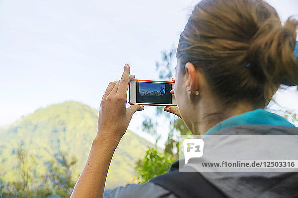 Nahaufnahme einer Frau  die mit ihrem Smartphone einen Berg fotografiert
