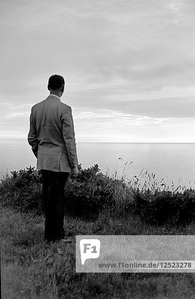 The silhouette of a man standing on a cliff top watching the sunset over the sea c1945-c1965. Artist: SW Rawlings