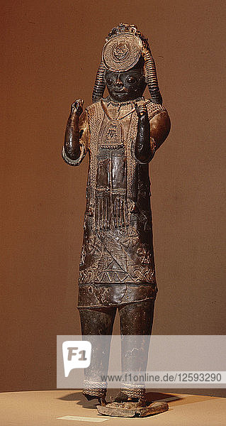 Eine große Figur  eine der Tsoede-Bronzen  die ein mit Kaurimuscheln bedecktes Obergewand  eine Halskette aus Leopardenzähnen und ein Brustschild mit Darstellungen eines Widders und von Vögeln trägt.