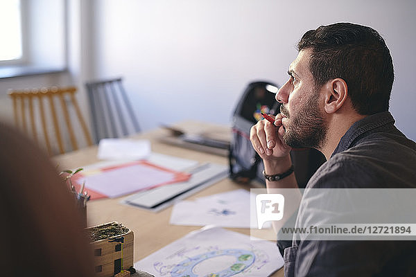 Side view of male engineer thinking while sitting with diagram at table in office