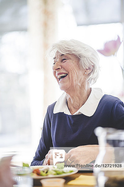 Cheerful senior woman having lunch at table in nursing home