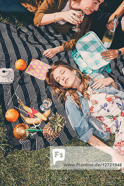 High angle view of young woman lying by friends enjoying picnic during summer at back yard