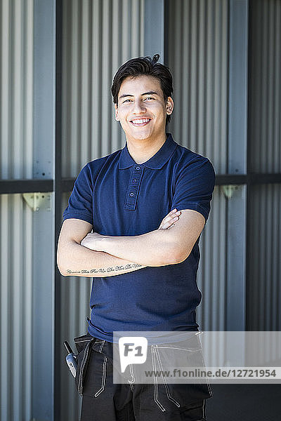 Portrait of smiling young male worker standing with arms crossed on warehouse entrance