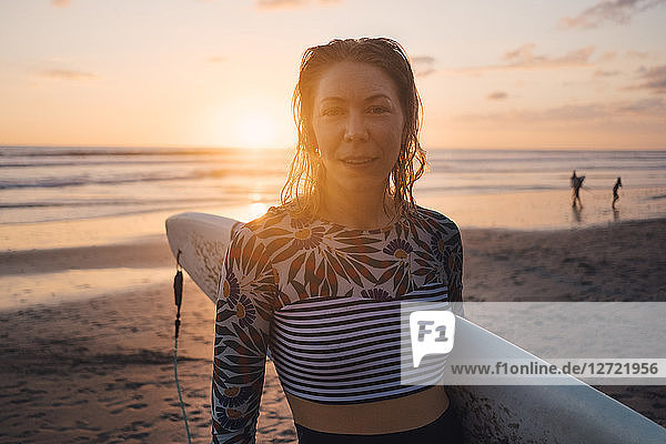 Portrait of mid adult woman with surfboard at beach during sunset