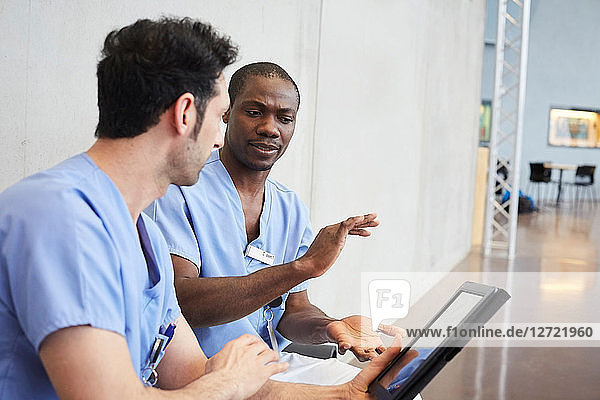 Male nurses discussing over digital tablet while sitting in corridor at hospital