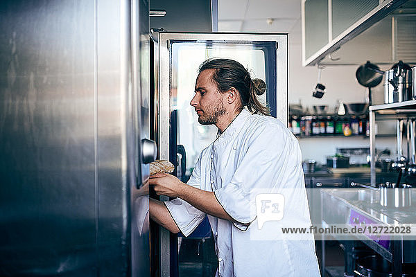 Male chef putting bread in oven at commercial kitchen