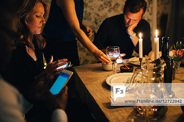 Mature friends using mobile phones while sitting at dining table in dinner party