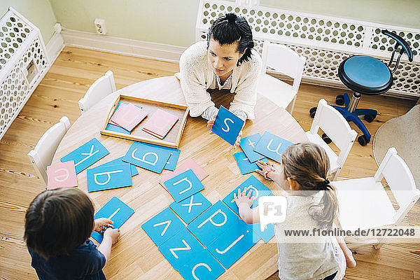 High angle view of confident female teacher showing letter S to students at table in classroom
