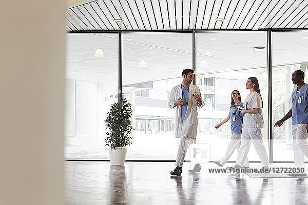 Full length of doctors and nurses discussing while walking in corridor against window at hospital