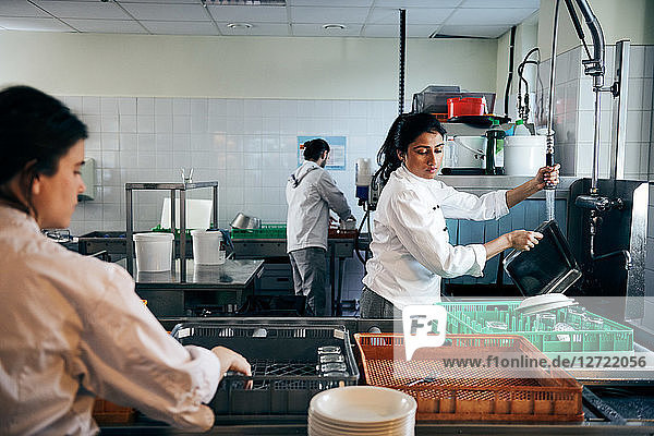 Female chef washing dishes in commercial kitchen