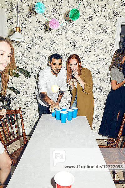 Confident young man playing beer pong on table by female friend at dinner party