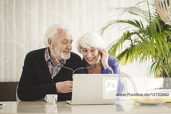 Cheerful senior couple using in-ear headphones while video calling through laptop in nursing home