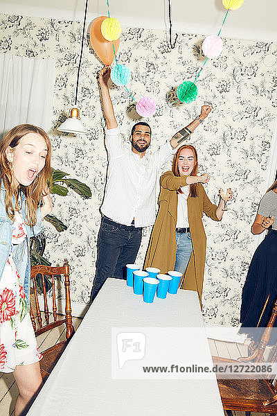 Happy young man with arms raised and female friends standing at dinner party